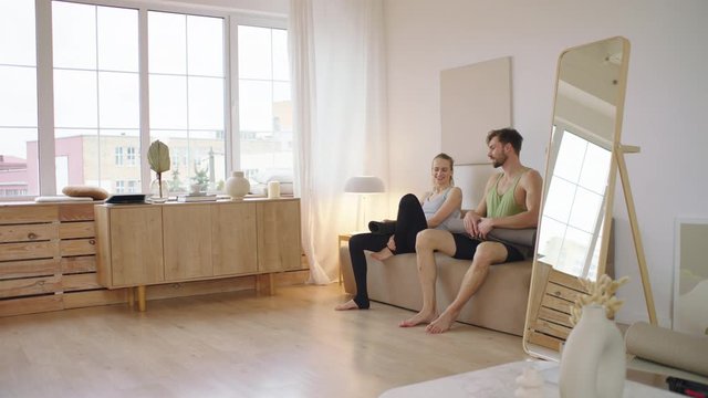 Fit young adult Caucasian couple living together practicing yoga at home. Girlfriend teaching boyfriend how to do yoga. Stay home, quarantine workout. Shot on ARRI Alexa Mini