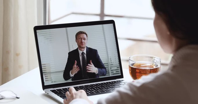 Smiling businessman boss wearing suit making video call conferencing with distance female worker, interviewing job applicant in home office webcam chat meeting on laptop screen. Over shoulder view