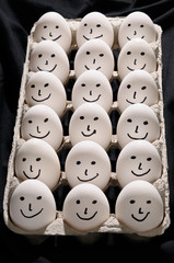 Package of backlit eggs on black cloth with whole group of smiling faces