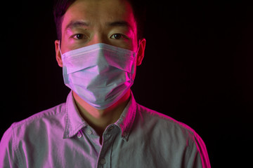 Portrait of asian young man. Chinese guy in medical mask against covid-19 Black background. Red backlight. Pandemic disease. Virus protection. Chinese coronavirus outbreak concept