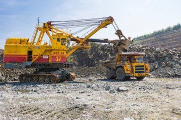 A mining excavator loads a huge truck with granite rock