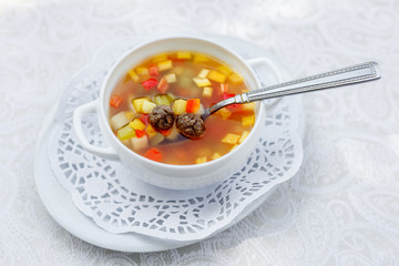 vegetable soup with meatballs in a white plate on a white tablecloth