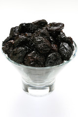 Glass bowl of shiny prunes on a white background