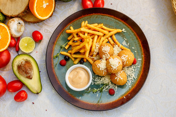 Crispy potato balls with soft melted cheese and french fries on decorated table