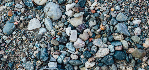 Gravel pattern of colored stones on the river coast. Texture of various pebbles, abstract background, top view.