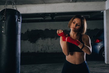 Young beautiful female preparing her bandages for kicking the boxing bag