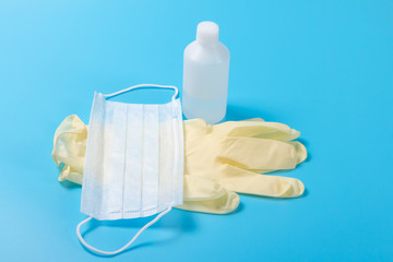Disposable medical mask, antiseptic and latex glove yellow on a light blue surface. The concept of virus protection