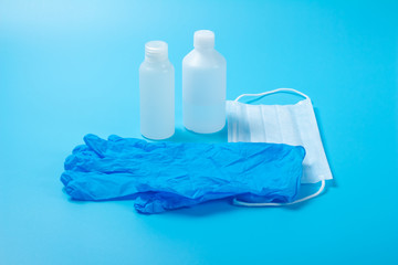 A disposable medical mask, two bottles of antiseptic and a blue latex glove on a blue background. The concept of virus protection