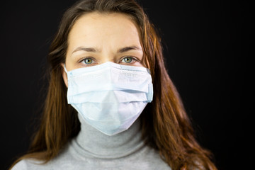Portrait of sexy woman with green eyes and long hair in medical mask close-up in studio. Girl in medical mask against viruses and infections. Coronavirus 2019-ncov covid-19 concept.