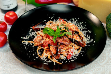 Italian pasta with parmesan cheese and seafood, with octopus, shrimps and mussels in a black plate on a white table