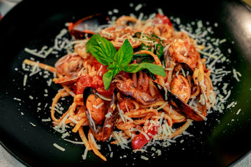 Italian pasta with parmesan cheese and seafood, with octopus, shrimps and mussels in a black plate on a white table