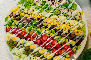 fresh salad with three kinds of meat, avocado, tomatoes and eggs on a white table