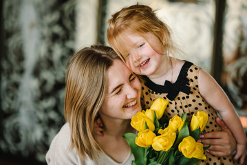 Mother's day concept. Cute little girl greeting mother and gives her a bouquet of flowers tulips at...