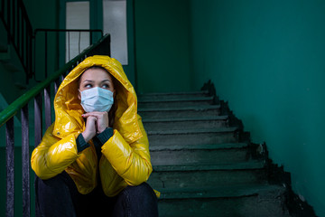 Caucasian girl in protective medical mask on face and in bright yellow jacket in abandoned building sits on the stairs. Wuhan is deadly epidemic. Quarantine due to Coronavirus. Copyspace.