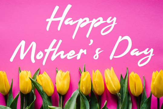 Happy mother's day. Text sign with yellow tulips on pink background.  Floral greeting card concept. Sensual tender women image. Holiday greeting card for Mother's Day! Top view, flat lay.