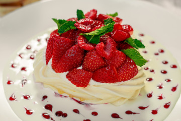 Pavlova dessert with cream mint and strawberry in a white plate on a white table