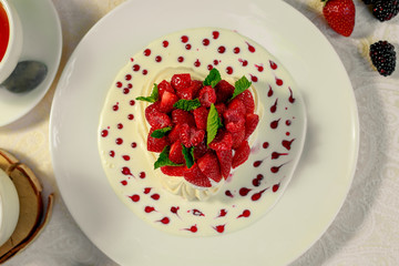 Pavlova dessert with cream mint and strawberry in a white plate on a white table