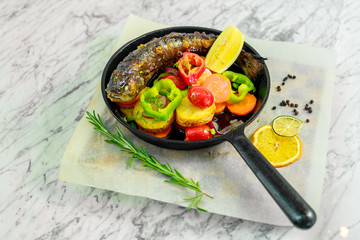 fried fish in a pan with rosemary and vegetables