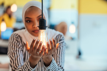 Sentimental portrait of African-American young female Muslim wearing hijab while holding a lightbulb.