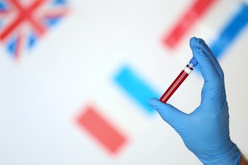 Coronavirus epidemic in the world. Coronavirus infection blood test.laboratory flask with blood and a hand in a blue  glove on the background of the flags of the world.Viral diseases statistics