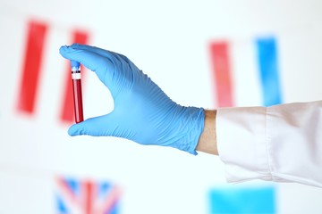 Coronavirus epidemic in the world. Coronavirus infection blood test.laboratory flask with blood and a hand in a blue medical glove on the background of the flags of the world. diseases statistics