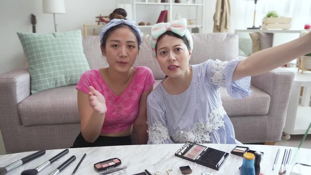 two attractive young female bloggers sitting in house living room preparing to start a live streaming video. group of girl friends moving camera to right place before recording beauty tutor channel