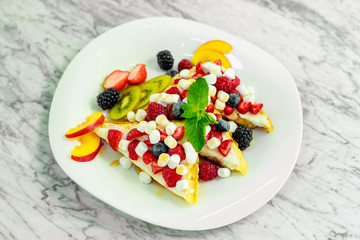 Belgian waffles with nuts, chocolate and fruit on a white plate, beautiful serving