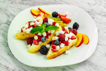Belgian waffles with nuts, chocolate and fruit on a white plate, beautiful serving