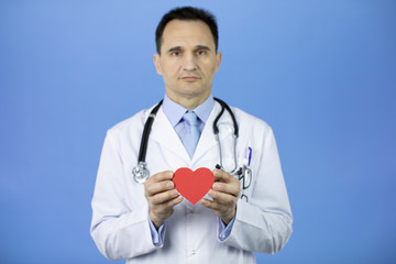 Caucasian cardiologist doctor with a stethoscope on a blue background holds a heart in his hands. Caring for people or patients. Heart disease treatment. Diseases of the cardiovascular system.