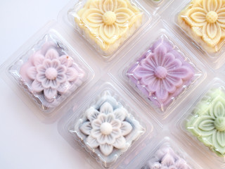 Top view of colorful snow lotus dessert, mooncake, bua hema in clear plastic box package isolated on white background.