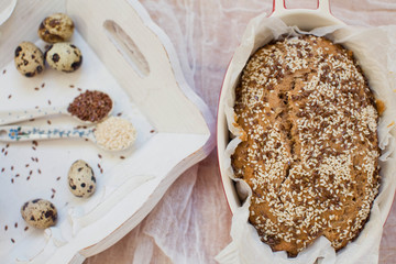 Whole wheat bread with sesame seeds and flax seeds in baking form. Fresh quail eggs, seeds and flour on a wooden tray