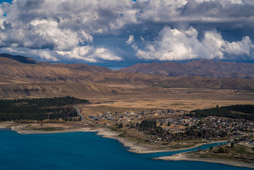 Obraz premium Scenic view from Mt St John Mountain Lake, with a view of the grassy hill, blue Lake Tekapo and the snow capped mountains in the background in Lake Tekapo in New Zealand South Island