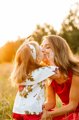 Little daughter kisses mom in a field at sunset..