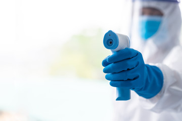 Medical worker scanning with infrared thermometer, IR Thermoscan, Confident doctor in protective PPE suit wearing face mask and eyeglasses in hospital