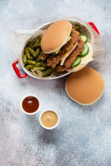 Serving tray with chicken strips burger, pickles and dips on a beige stone background, top view with space, vertical shot