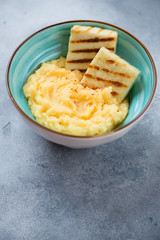 Turquoise bowl with polenta and fried cheese, studio shot on a light-blue stone background with space