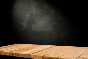 Old wood table with blurred concrete block wall in dark room background.