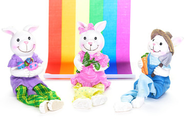 Three cute porcelain bunny rabbits ready for the Easter holiday, in front of a rainbow flag