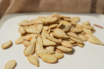 Many pumpkin seeds are gathered together on a white container.
