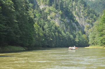 Fototapeta na wymiar Rafting on the Dunajec River in the Pieniny National Park on wooden folding shuttles tied with a rope. Rafters paddling on a rapid stream with a rocky bottom and strong river current.