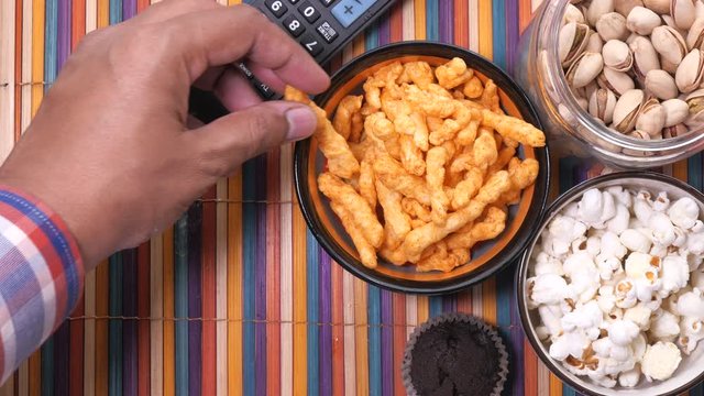 A bowl of popcorn chips, nut and TV remote,