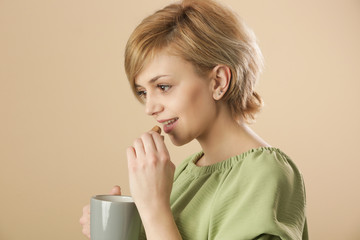 Studio shot of happy young woman holding cup of coffee and eating chocolate chip cookie