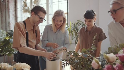 Zoom in shot of young man cutting decorative green twig and putting it in hat box with assistance of professional female florist during masterclass in flower workshop