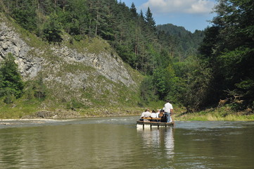 Rafting on the Dunajec River in the Pieniny National Park on wooden folding shuttles tied with a rope. Rafters paddling on a rapid stream with a rocky bottom and strong river current.