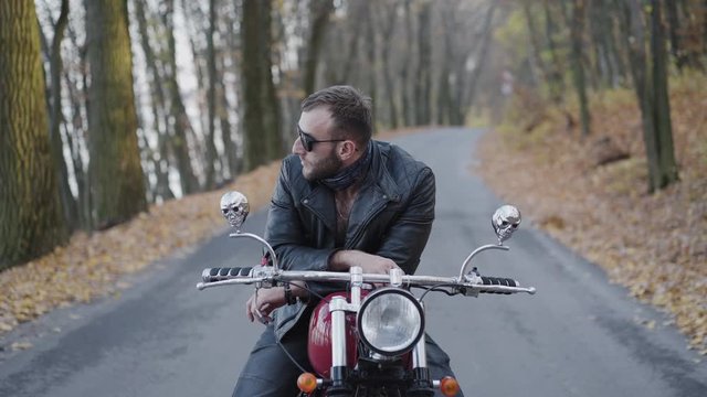 Portrait of brutal biker behind a motorcycle stands and thinks among roadway