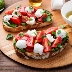 Bruschetta with cherry tomatoes,  mozzarella cheese and pesto sauce on wooden board. Traditional italian appetizer or snack, antipasto.