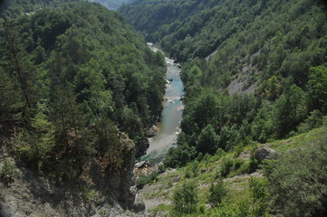 Fototapeta na wymiar The bridge on the Tara River in Montenegro and the bridge connecting the two banks of the canyon. A stony bed of a clean river flowing through the valley along the road on a mountain slope.