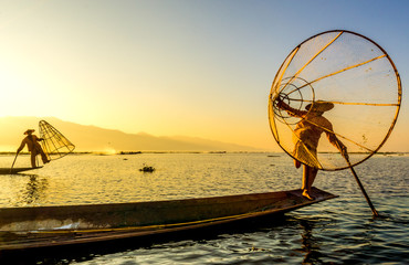 Myanmar travel attraction landmark - Traditional Burmese fishermen with fishing net at Inle lake in Myanmar famous for their distinctive one legged rowing style