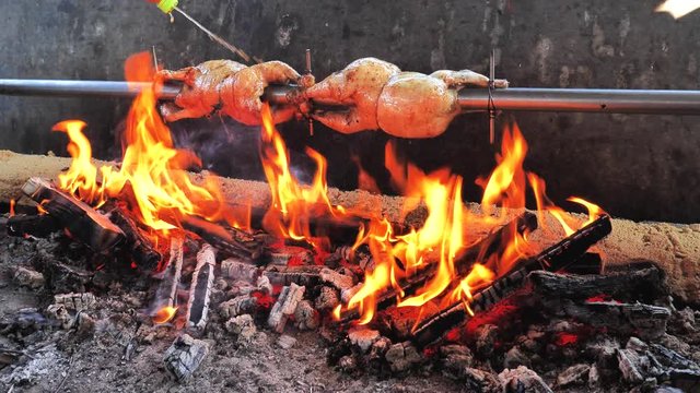 Man chef spray spicy marinate on roast Chicken on the BBQ steel bar in bricks built grill furnace.