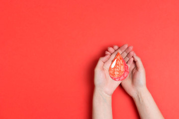 Fototapeta na wymiar Human hands holding blood drop symbol on red background with copy space. Blood donation.